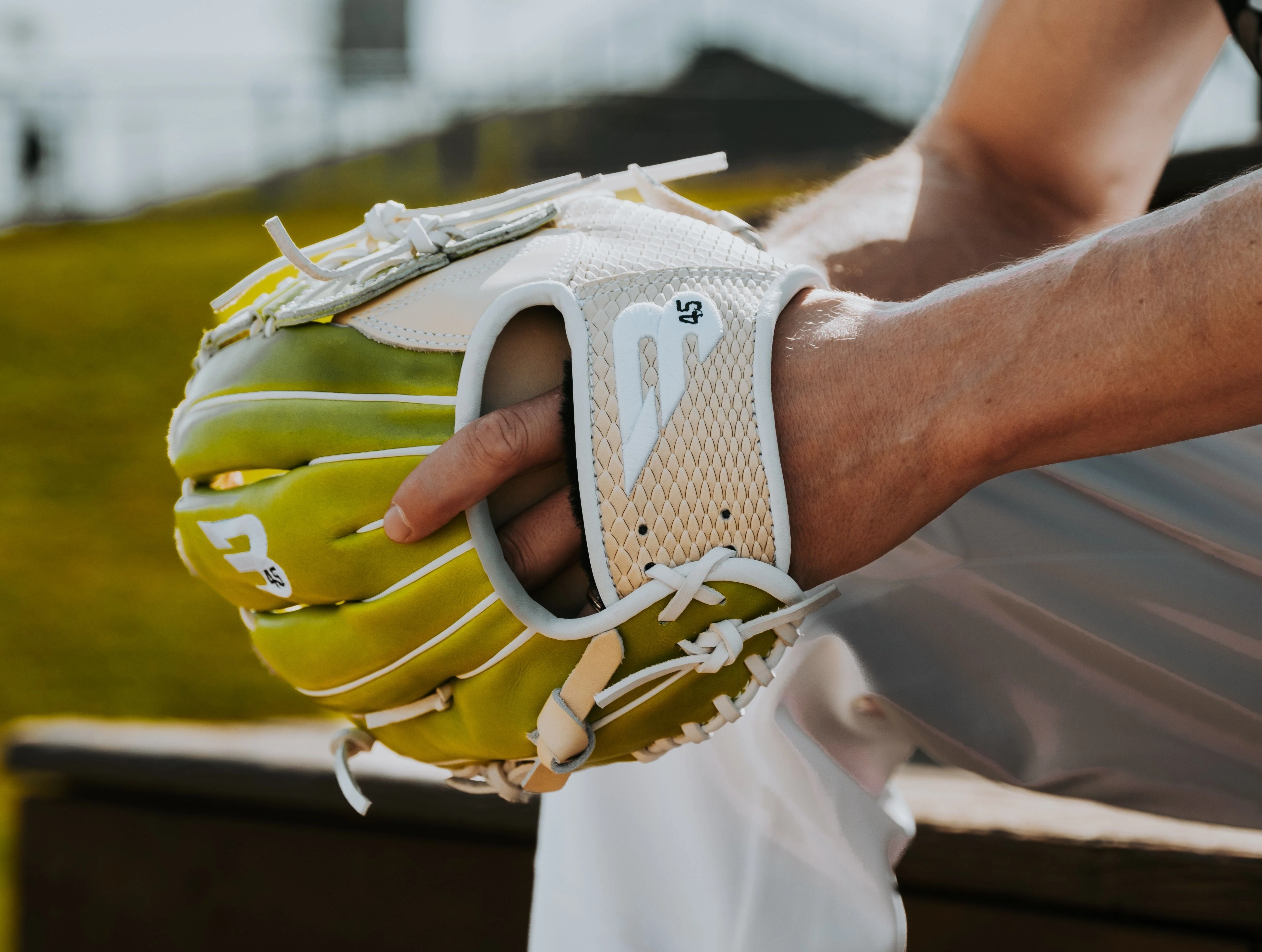 Hands using a small soft-bristle brush to clean dirt from the laces and seams of a leather baseball glove on a workbench