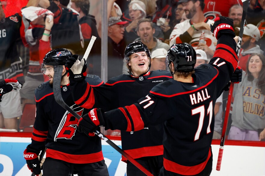 Hockey players celebrating a goal near the boards during a playoff game.