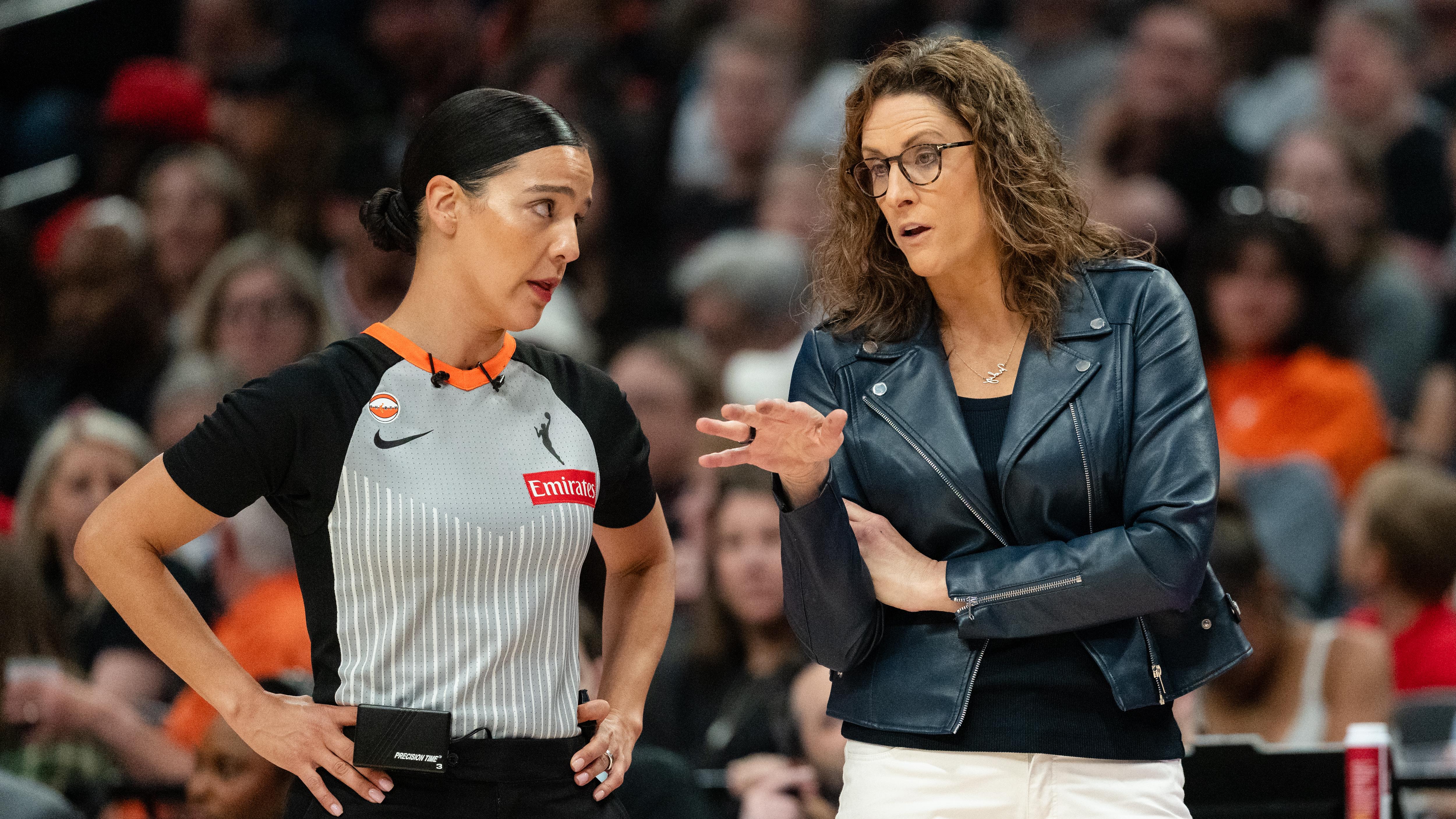 Indiana Fever head coach Stephanie White standing near the sideline during a game, gesturing toward the court while speaking to an official as play continues