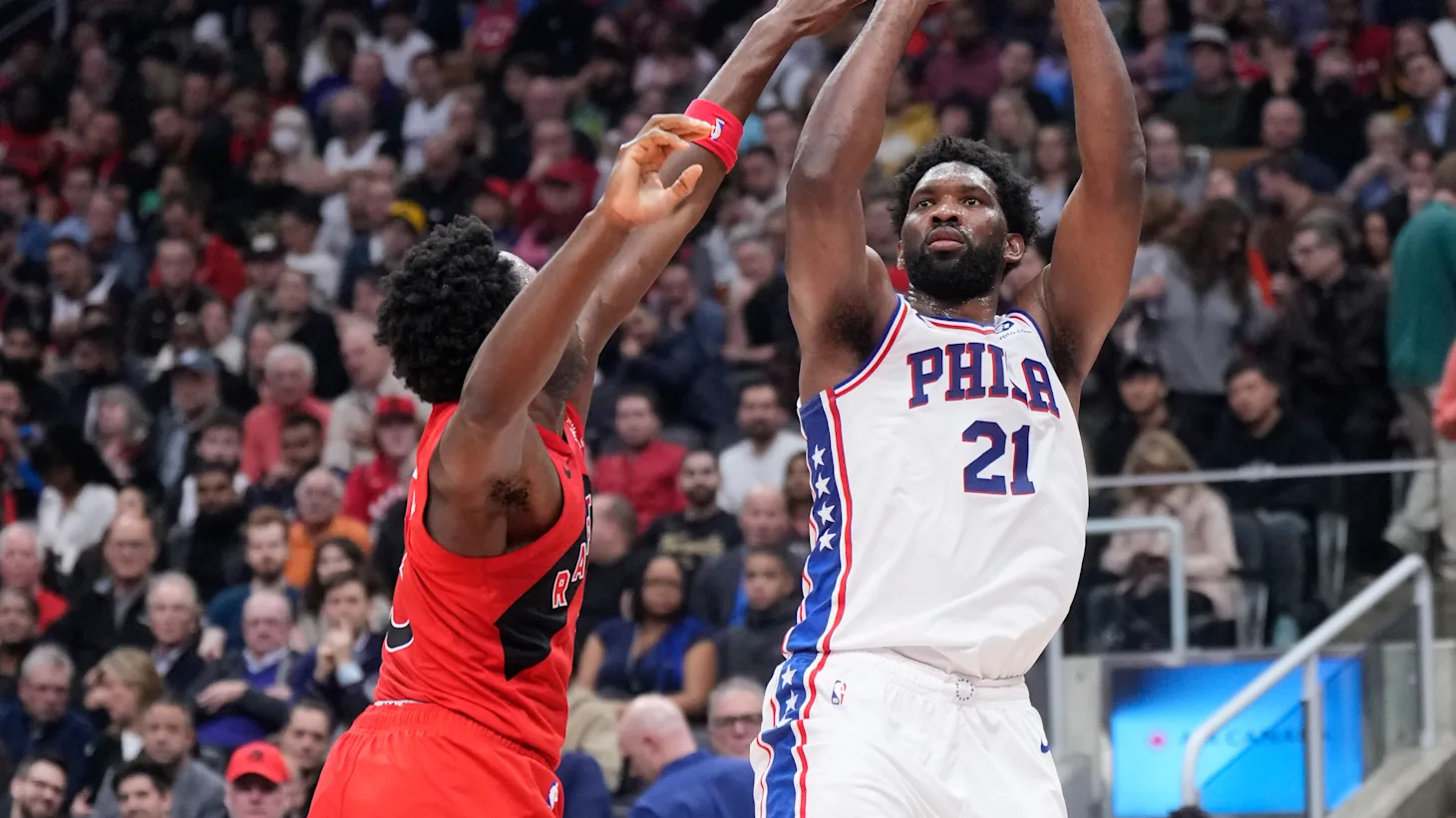 Joel Embiid on the court during a Philadelphia 76ers home game, set in a half-court possession with teammates spaced around him