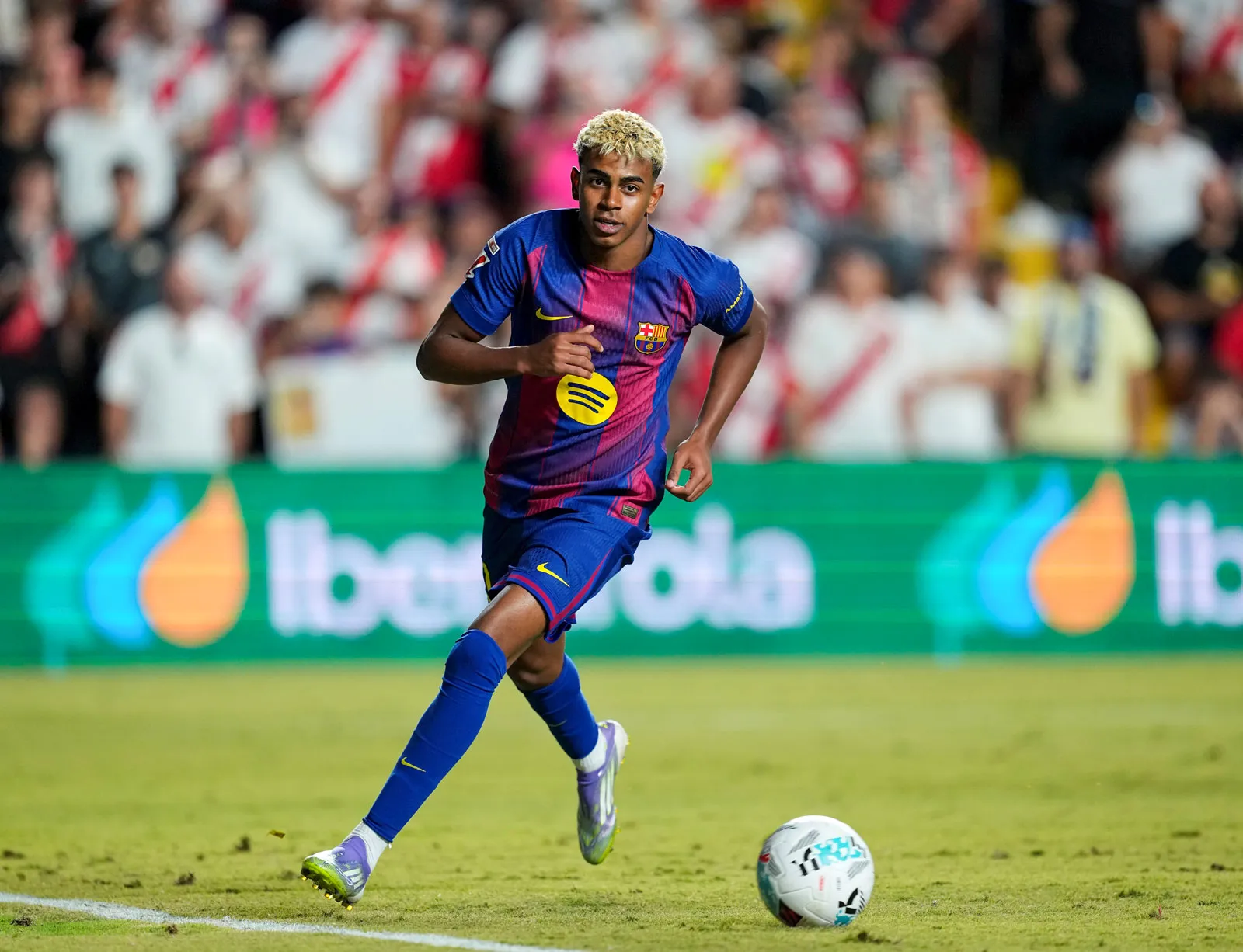 Lamine Yamal in an FC Barcelona kit dribbling down the right wing during a match, with a defender tracking back