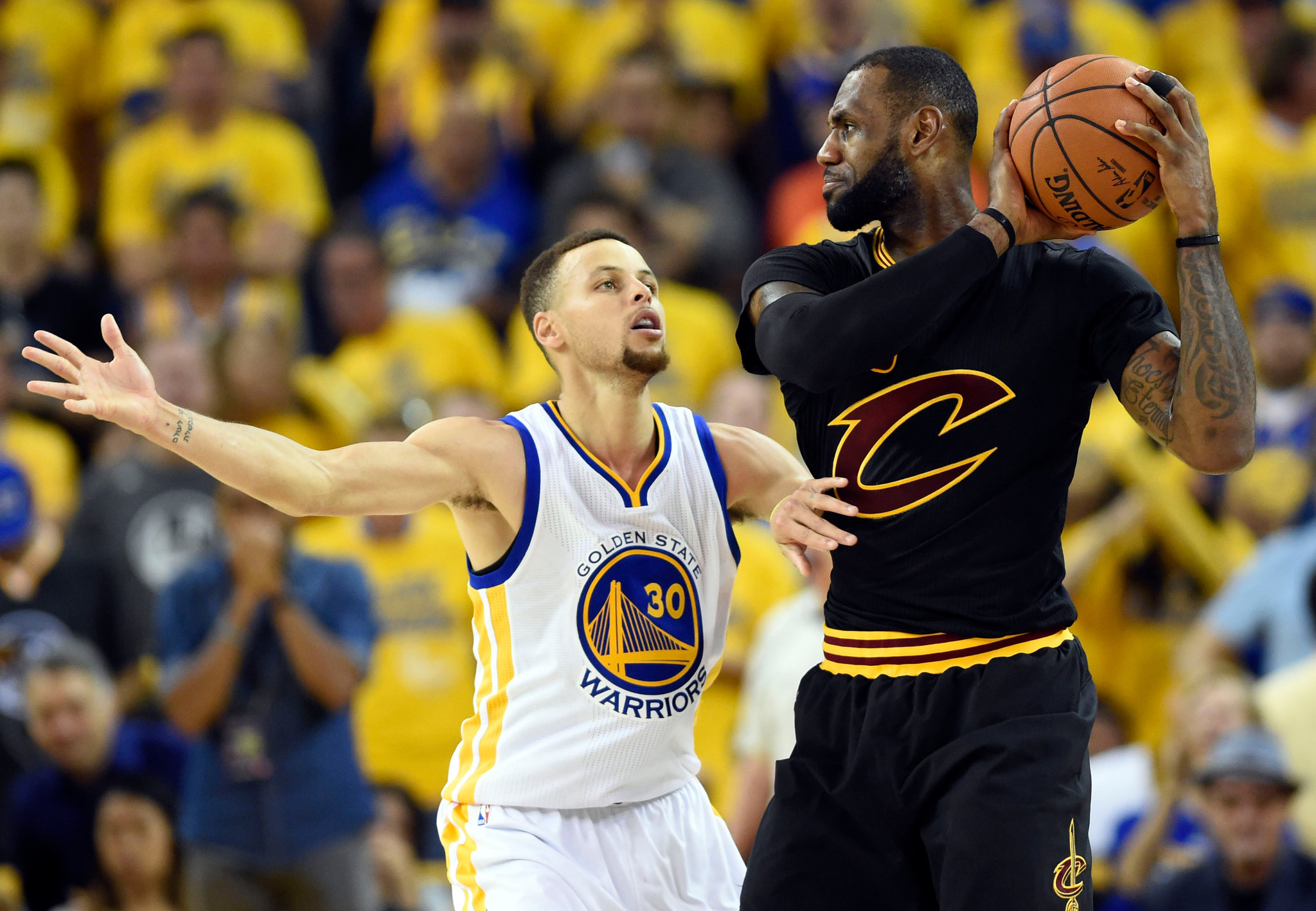 LeBron James in a Cleveland Cavaliers uniform driving toward the basket in an NBA Finals game with multiple defenders in the paint and bright arena lights overhead