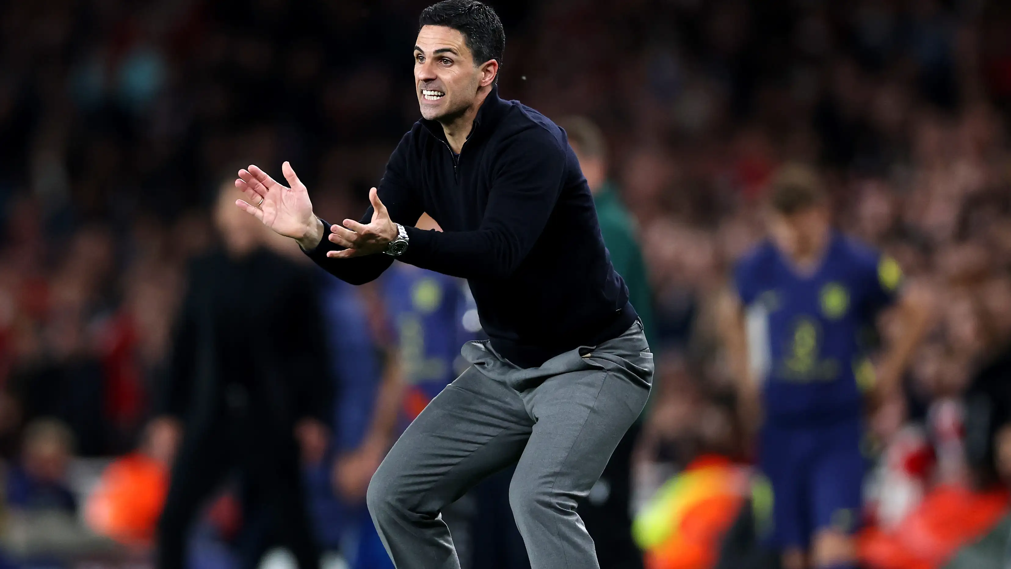 Mikel Arteta on the touchline during a Premier League match, gesturing instructions toward his players as the crowd watches