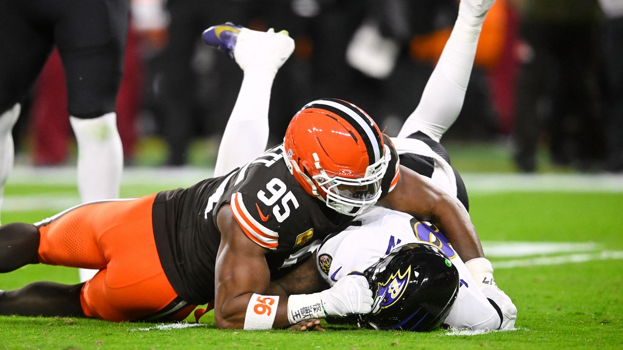 Myles Garrett wrapping up a quarterback for a sack as offensive linemen reach to pull him back