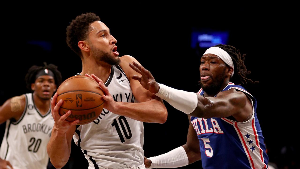 Players and coaches stand quietly as medical staff attends to an injured player during a stoppage in a 76ers vs Nets preseason game