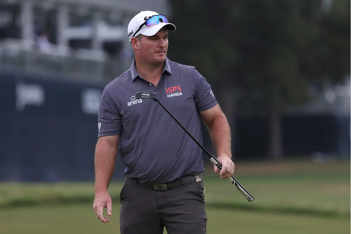 Ryan Fox lining up a putt on a Royal Birkdale green during the 2026 Open Championship, crouched behind the ball with the grandstands in the background