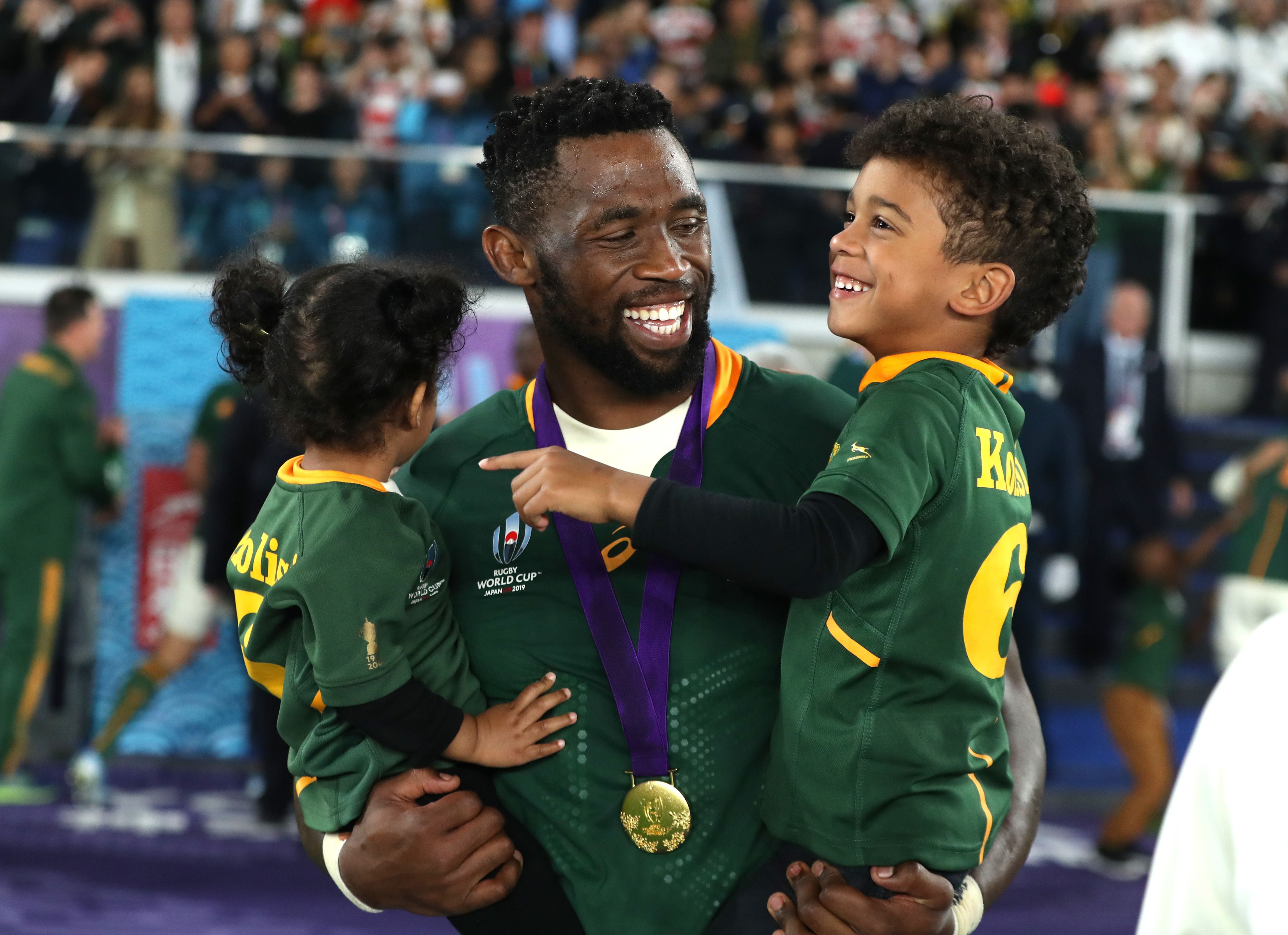 Siya Kolisi lifting the Rugby World Cup trophy in 2019 with teammates celebrating behind him and confetti in the air