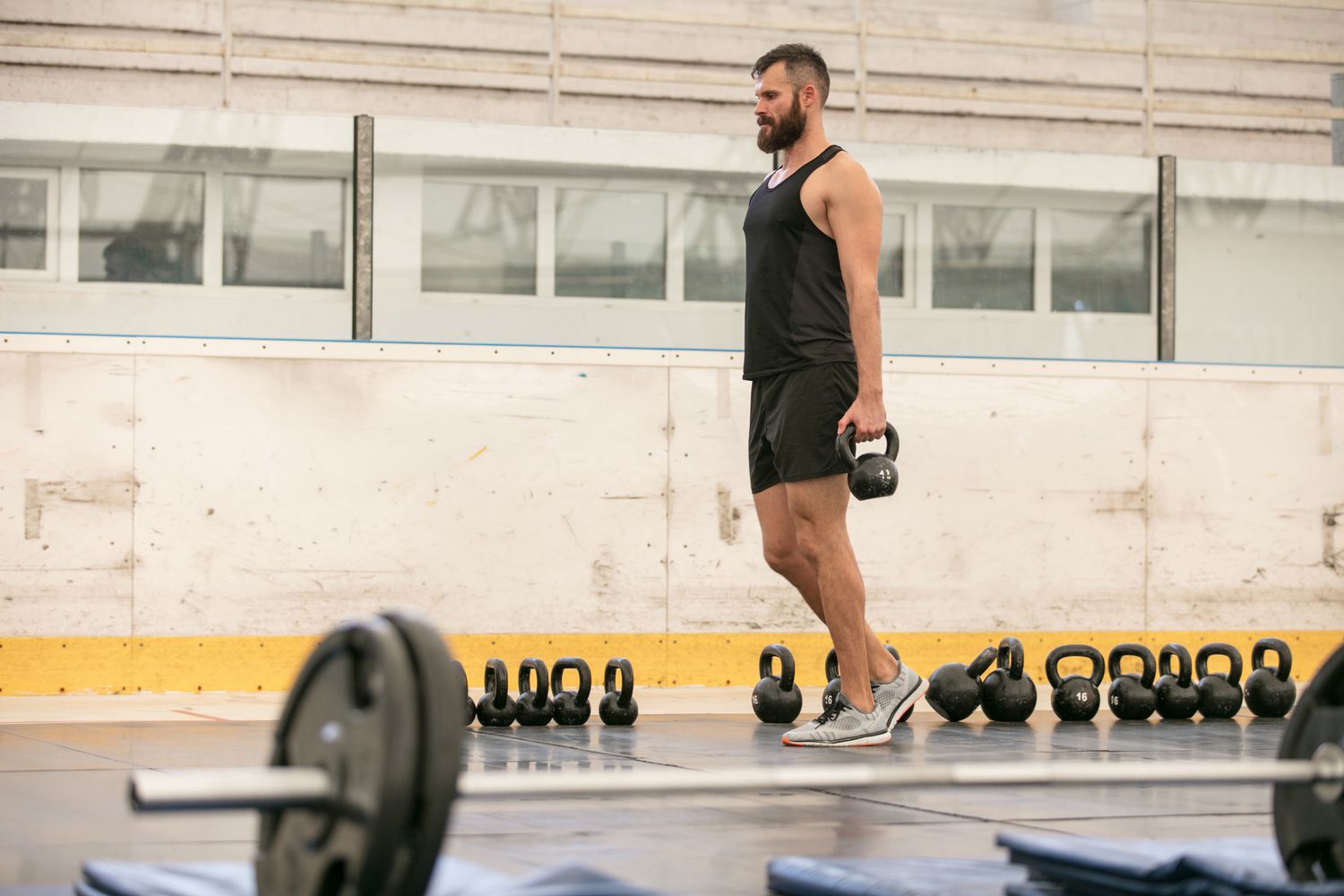Strength athlete walking with a heavy kettlebell in one hand during a suitcase carry, shoulders level and torso upright