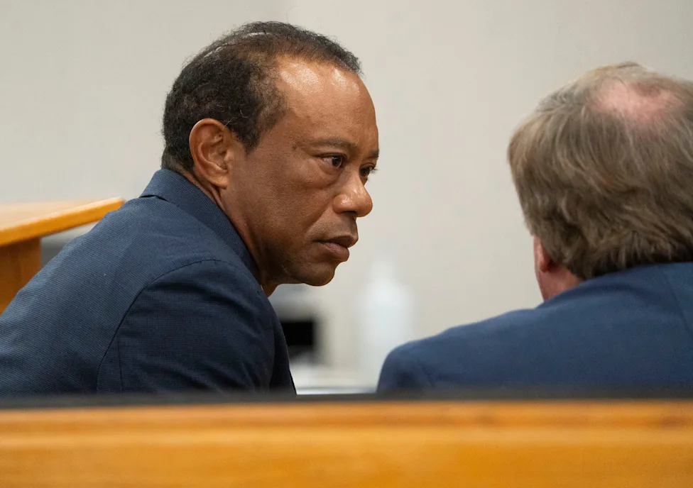 Tiger Woods wearing a suit and tie outside a Florida courthouse, walking past cameras and reporters, news photography style