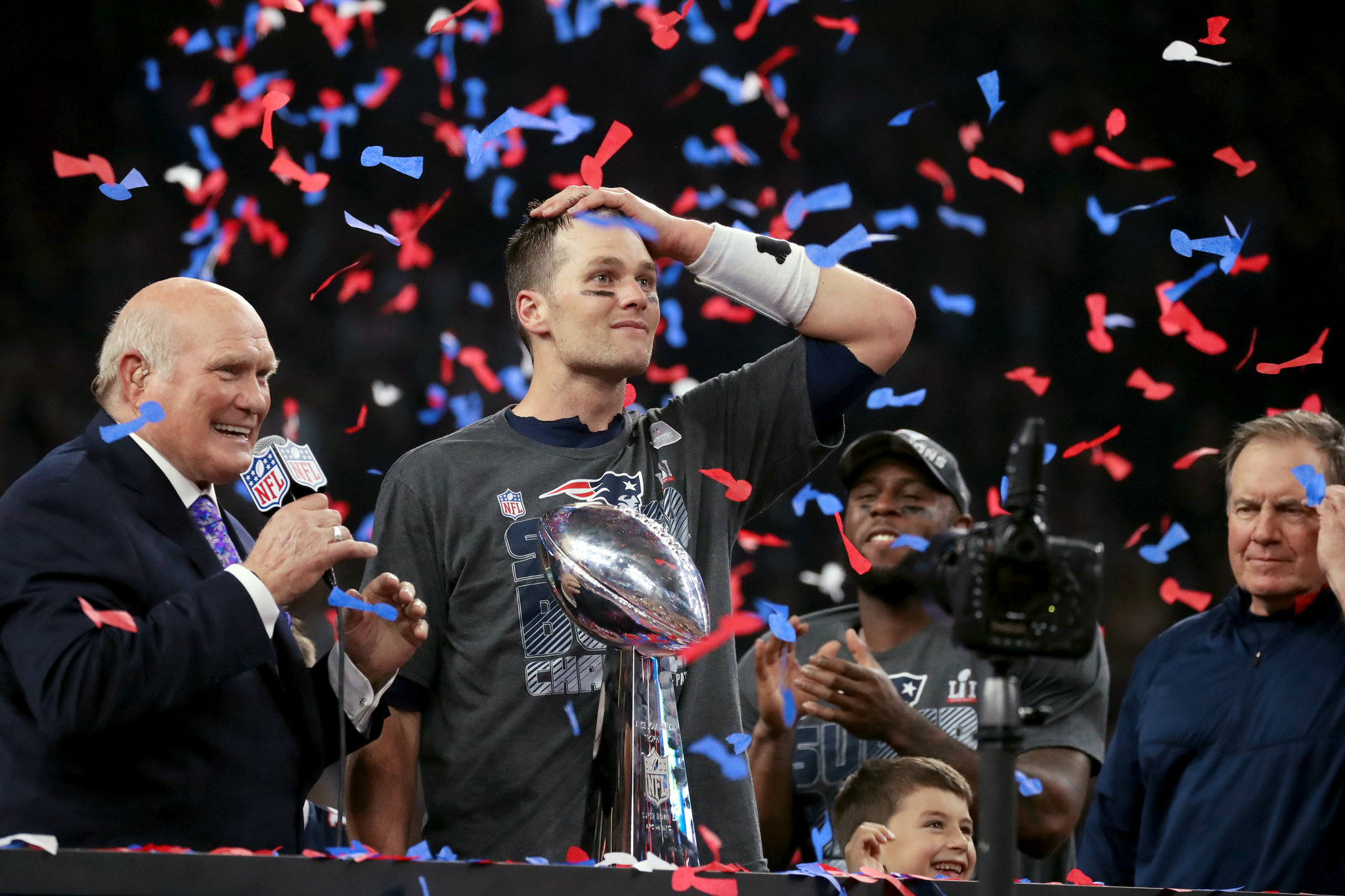 Tom Brady in the pocket during a late-game Super Bowl drive, scanning downfield with linemen engaged at the line of scrimmage