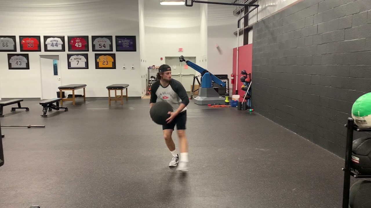 Training athlete performing a rotational medicine ball scoop toss into a wall in an indoor gym, captured mid-throw
