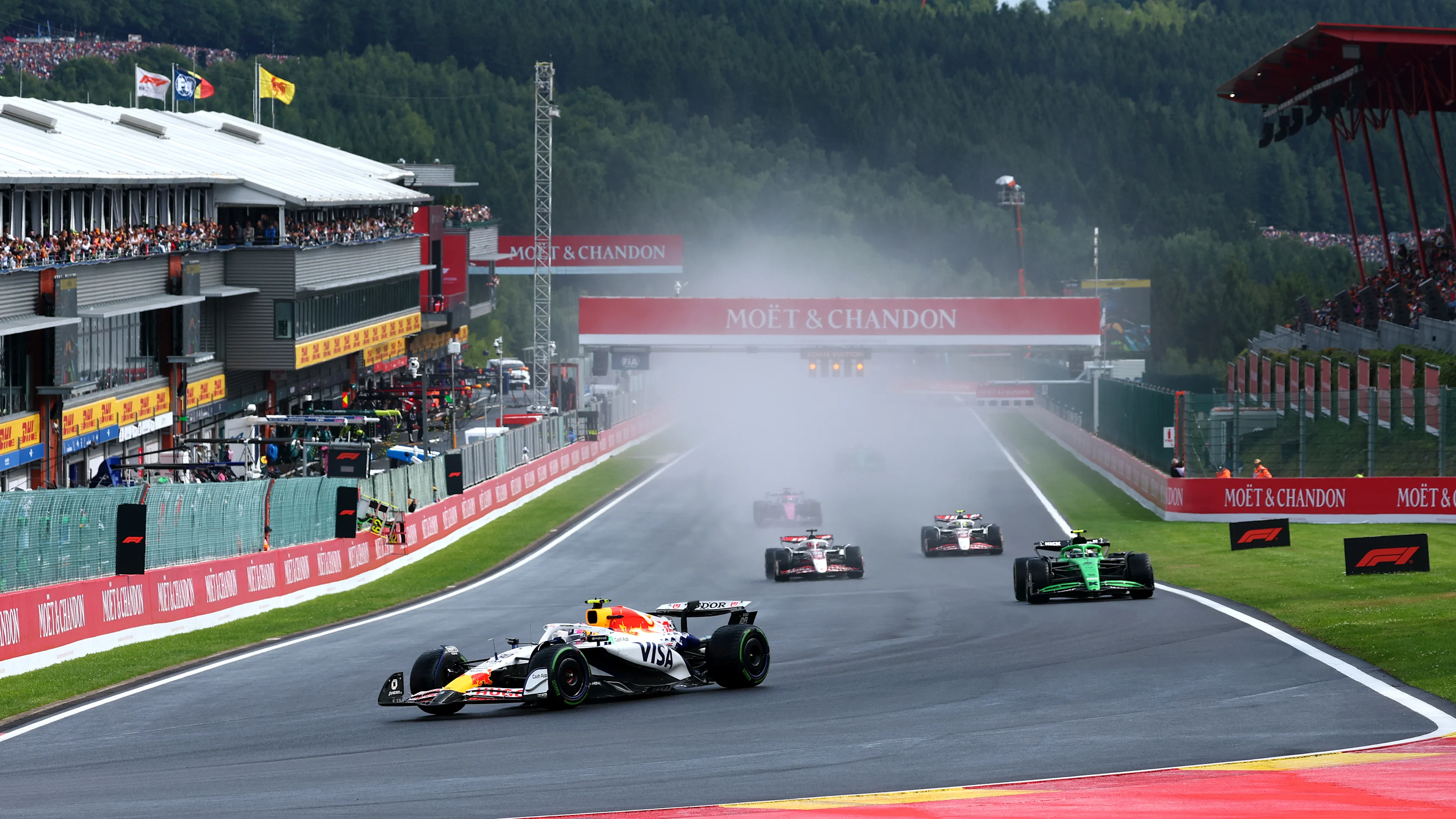 Two Formula 1 cars run close together on the Kemmel Straight at Spa, with the trailing car benefiting from slipstream